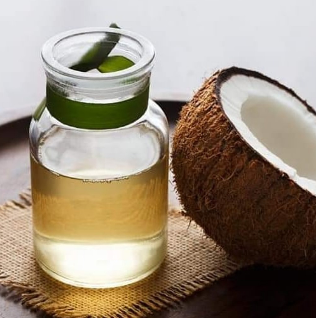 Pure coconut oil is stored in a glass bottle and a bowl, with a coconut placed nearby. Swadish Foods All Products.