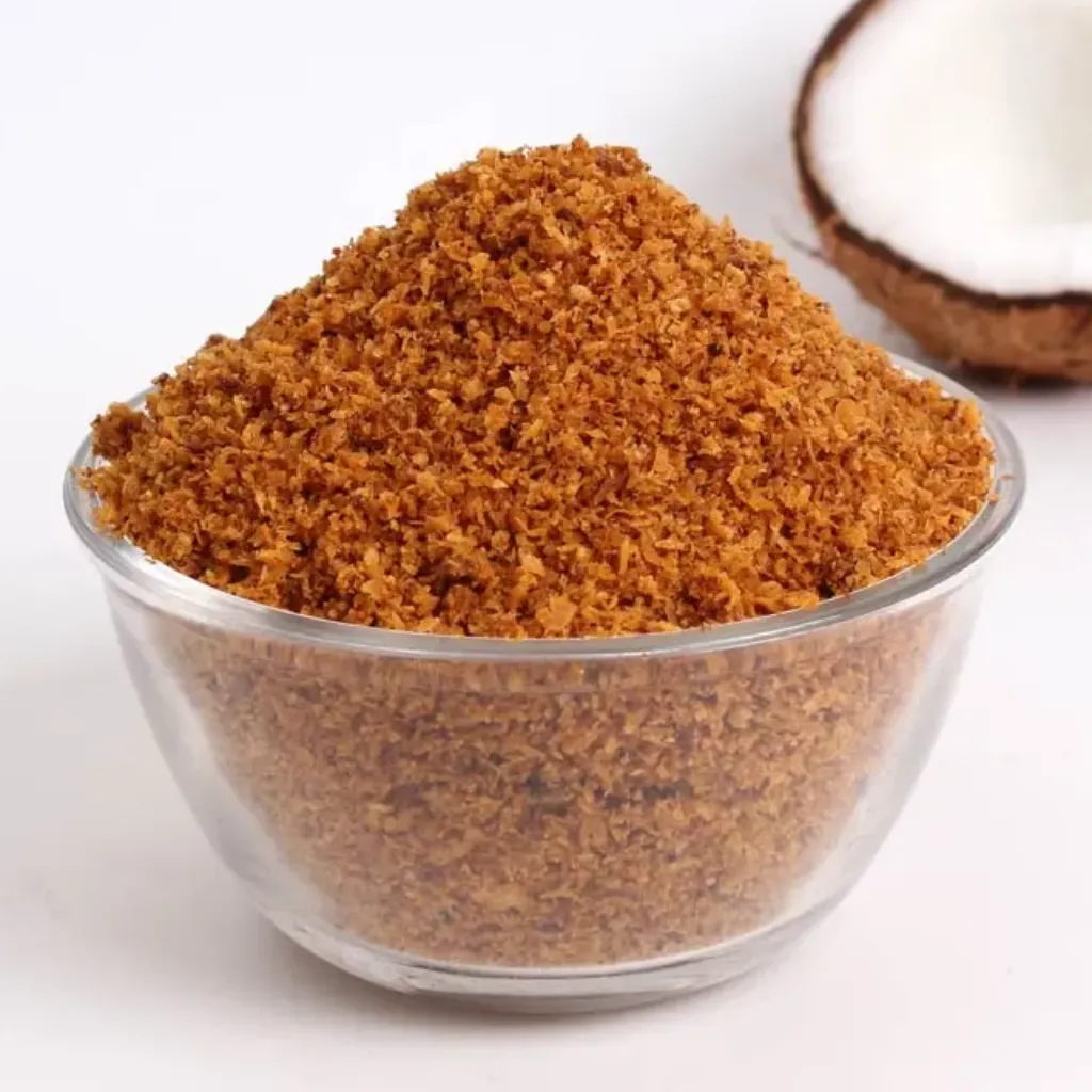 A bowl of coconut chammanthi powder nearby half cut coconut against a white background. Chammandhi podi