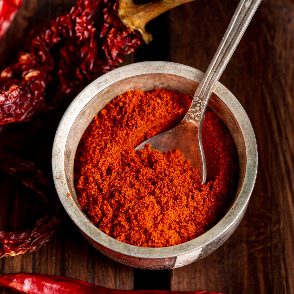 Chili powder is in a bowl placed nearby red chilies.